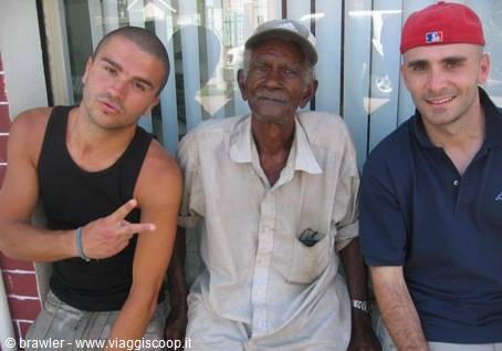 Two smiling young tourists beside a local elderly man in front of a shop window