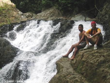 Two guys sitting on rock beside waterfall in tropical forest