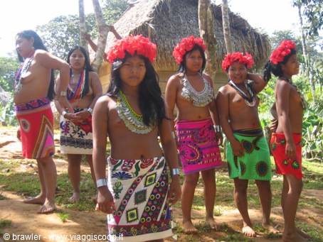 Emberá women in colorful skirts and red flower crowns by thatched hut