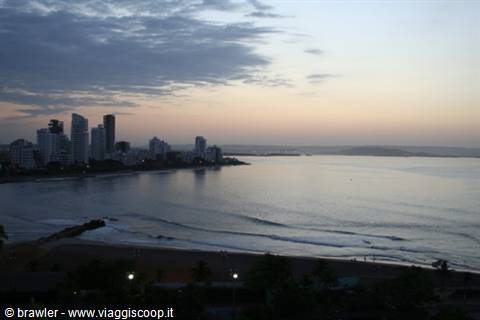Skyscrapers over the bay at dawn, ocean waves and lit lamps on the beach