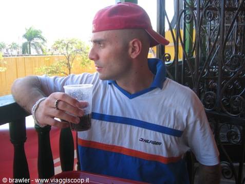 Man in red cap and white shirt drinking from a plastic cup on a balcony