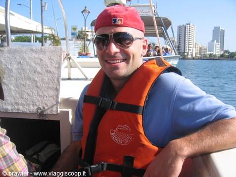 Man in red cap and orange life jacket on a boat near harbor towers