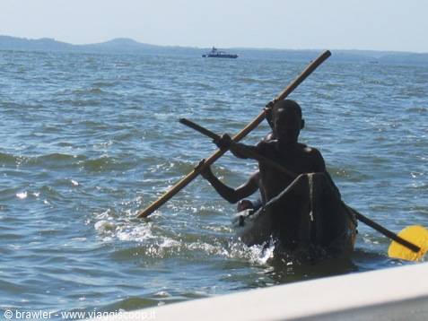 Boy paddling a dugout canoe with a wooden pole at sea