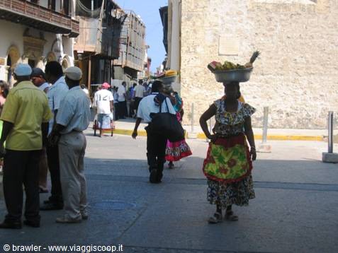 Woman carrying fruit basket on head walks Cartagena's colonial street