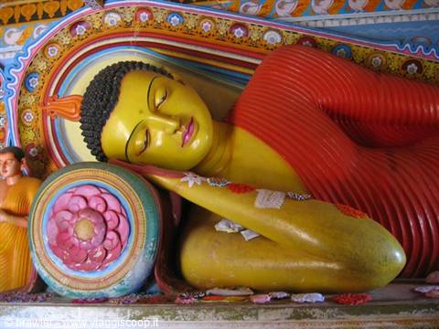 Large reclining Buddha statue painted yellow and red, resting on a floral cushion