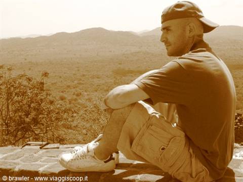 Traveler in a cap sitting on a stone wall facing dry hills