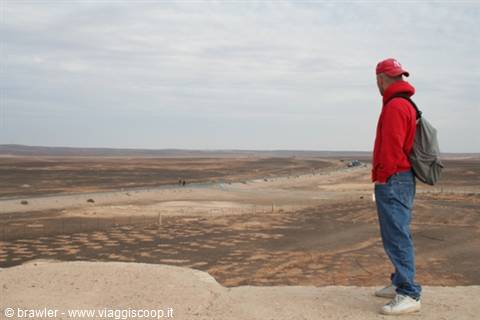 Tourist in red sweatshirt with backpack gazes at rocky desert under cloudy sky