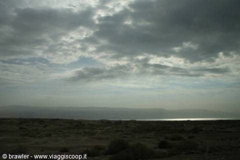 Cloudy sky over rocky desert, a silvery strip of water on the horizon