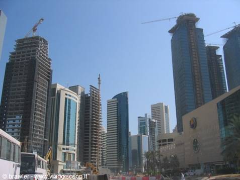 Skyscrapers under construction in Doha, cranes and glass towers under blue sky