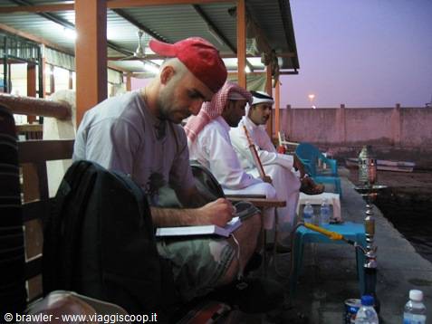 Traveler in red cap writing in notebook beside men in traditional dress, shisha on the waterfront