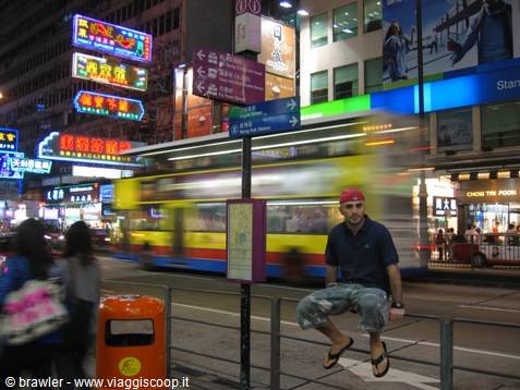 Tourist sitting on a railing at Nathan Road, Hong Kong, blurred moving bus and neon signs