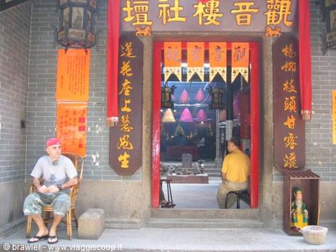 Man sitting at Kwun Yam temple entrance, red banners and lanterns