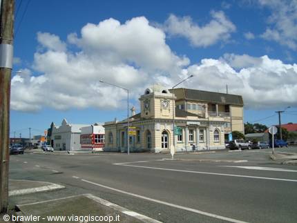 Historic clock building on a street corner, parked cars, cloudy sky
