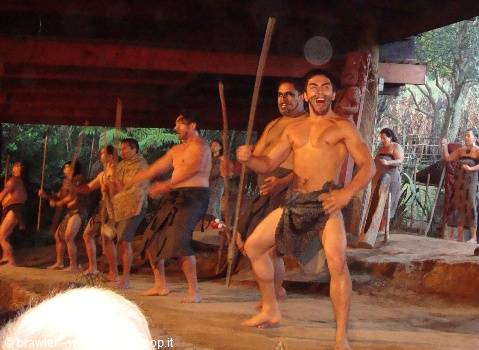 Men performing haka with spears under wooden shelter at Mitai Village, Rotorua