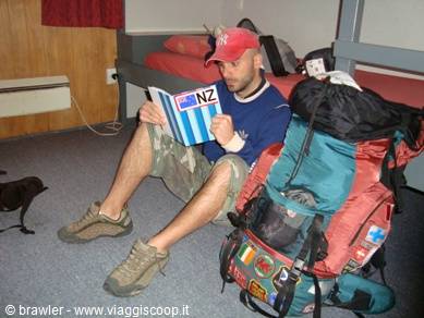 Backpacker with large hiking pack reads a New Zealand guidebook on a bunk bed