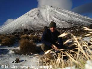 Hiker crouching in snow before the snow-capped Mount Ngauruhoe volcano