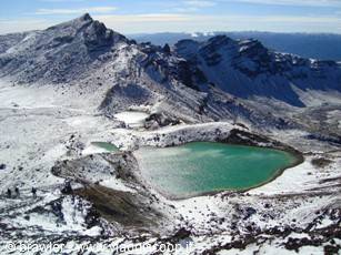 Turquoise lake surrounded by snow and volcanic rocks, snowy mountains behind