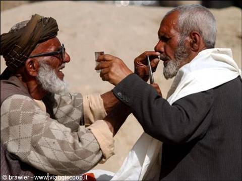 Two elderly bearded men share a small glass outdoors