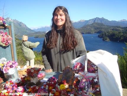 Woman smiling among wool crafts at stall, blue lake and mountains behind
