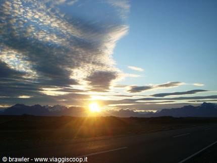 Sunrise behind mountains, cloudy sky, dark asphalt road in foreground