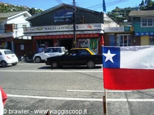 Chilean flag waving over a street with taxis, parked van and shops