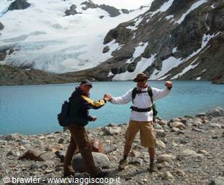 Two hikers high-five by a turquoise glacial lake amid snow patches