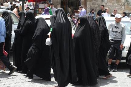 Women in black chadors walk through a busy street in Damascus