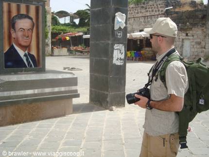 Photographer with backpack in front of Hafez al-Assad portrait on black basalt