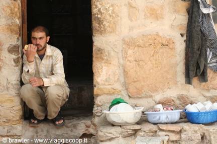 Man crouching in stone doorway eating bread, plastic baskets beside him