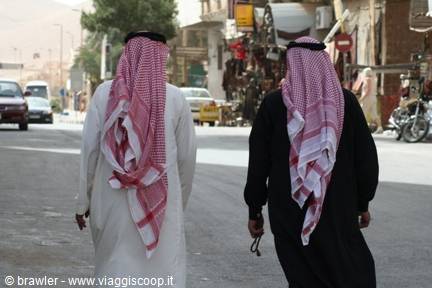 Two men wearing red checkered keffiyeh walk down a street, Wadi Musa
