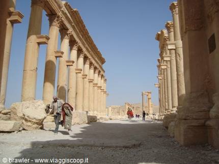 Sandstone colonnade at Palmyra, tourists walk between ancient columns under the sun