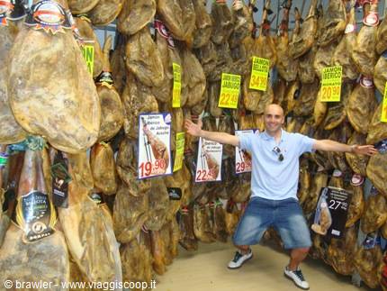 Man in blue t-shirt and denim shorts among hundreds of hanging hams in shop