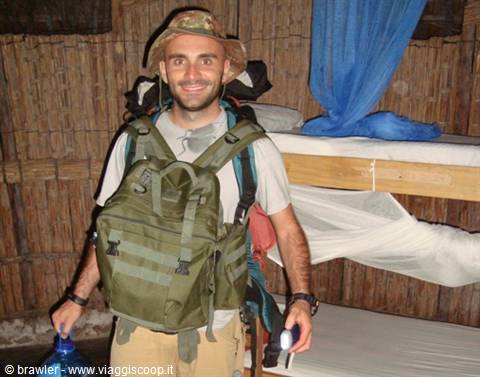 Smiling traveler with green military backpack and hat inside a bamboo hut