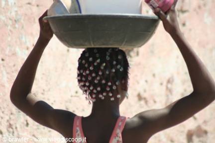 Woman with beaded hair balancing a plastic basin on her head