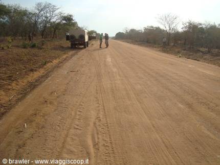 Travelers beside a loaded 4x4 on a dirt road among dry trees
