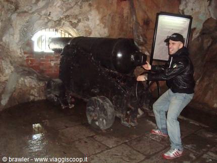 Tourist beside an old black cannon inside a rock-hewn tunnel