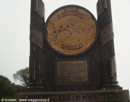 Bronze monument with carved medallion under grey rainy sky
