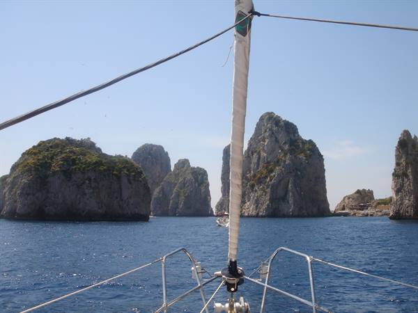 From a sailboat deck, the Faraglioni rocks of Capri rise over blue sea