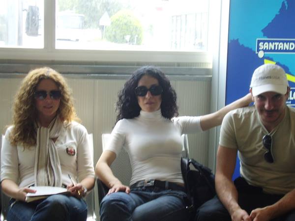Three people wearing sunglasses sitting on chairs near a Santander branch