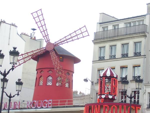 The red windmill of the Moulin Rouge in Paris among lampposts and neon signs
