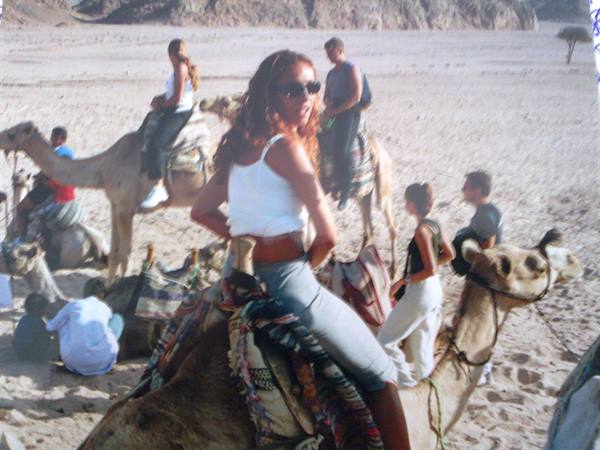 Tourist in white top riding a camel among sandy dunes
