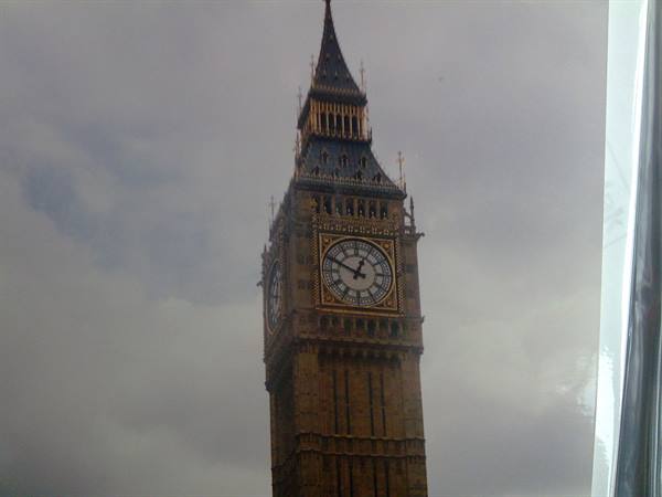 Big Ben in London seen through glass, golden stone tower under grey clouds