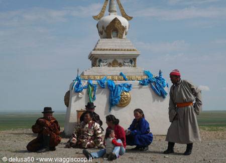 Nomad family in del beside a white stupa with blue ceremonial scarves