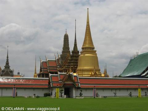 Golden stupa and red roofs of Wat Phra Kaew under cloudy sky