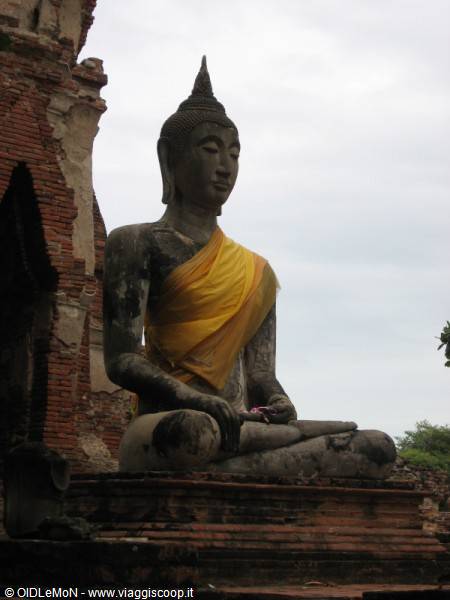Large seated stone Buddha draped in yellow cloth among brick ruins at Ayutthaya