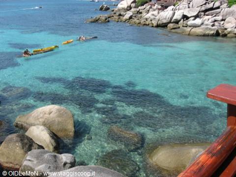 Yellow kayaks on turquoise water among granite boulders by rocky shore