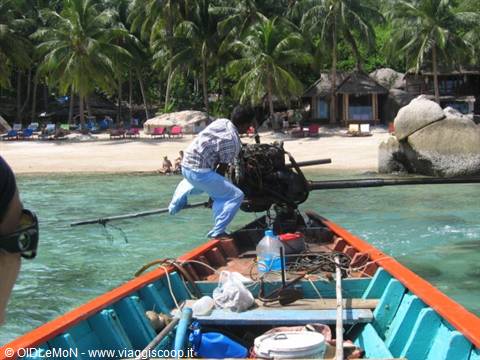 Blue wooden longtail boat near palm-lined beach, man adjusting the engine