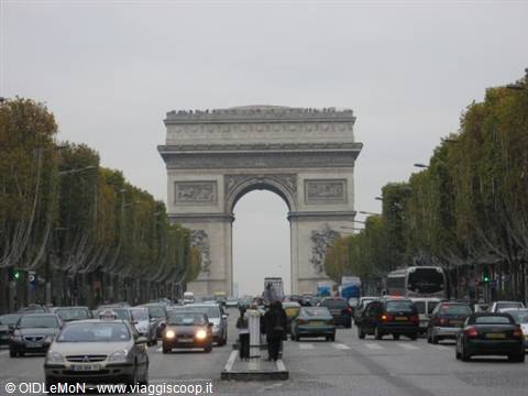 Arc de Triomphe from the Champs-Élysées, busy traffic and autumn trees under gray sky