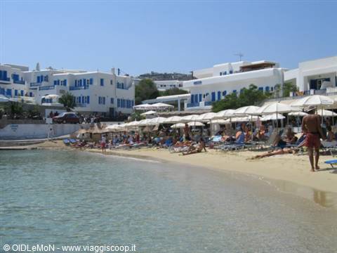Beach with umbrellas and sunbathers, white buildings with blue shutters behind