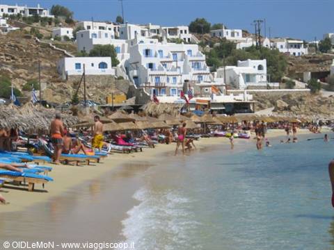 Tourists under straw umbrellas and sunbeds, white Cycladic houses behind, Mykonos